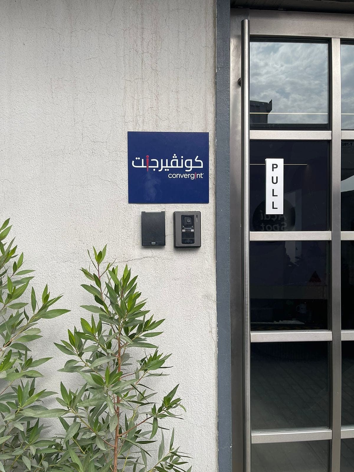 Blue bilingual Convergint name plate on a white wall beside a glass office entrance