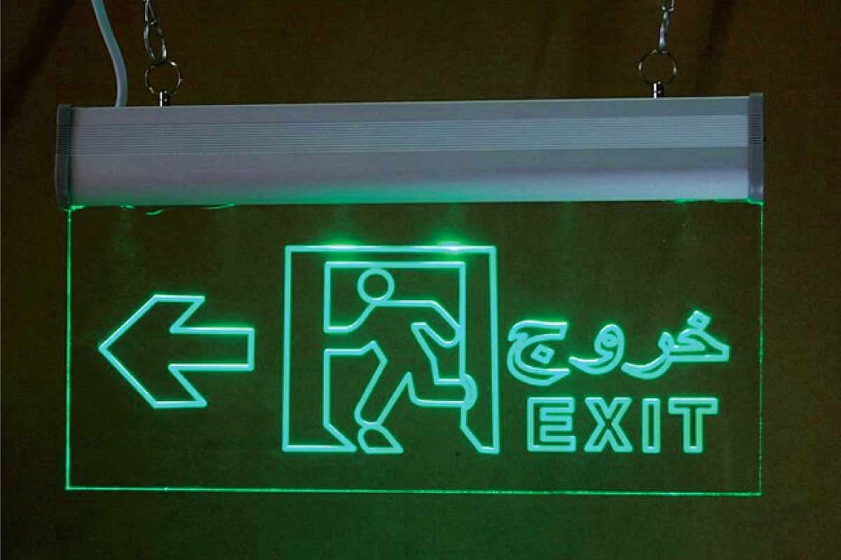Green edge-lit acrylic exit sign with a running-man pictogram and bilingual EXIT lettering, suspended from a ceiling