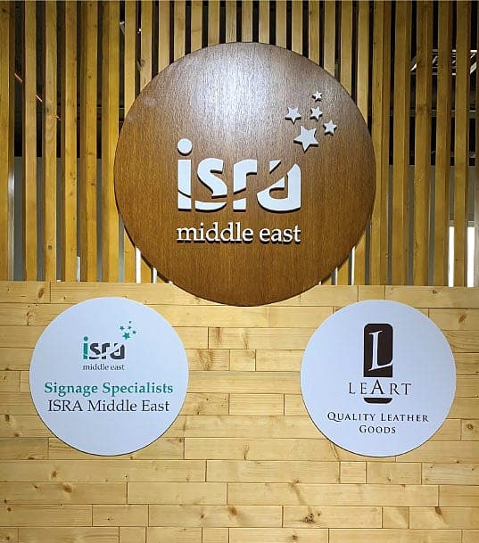 Round wooden Isra Middle East sign with two engraved acrylic discs on a slatted wood wall