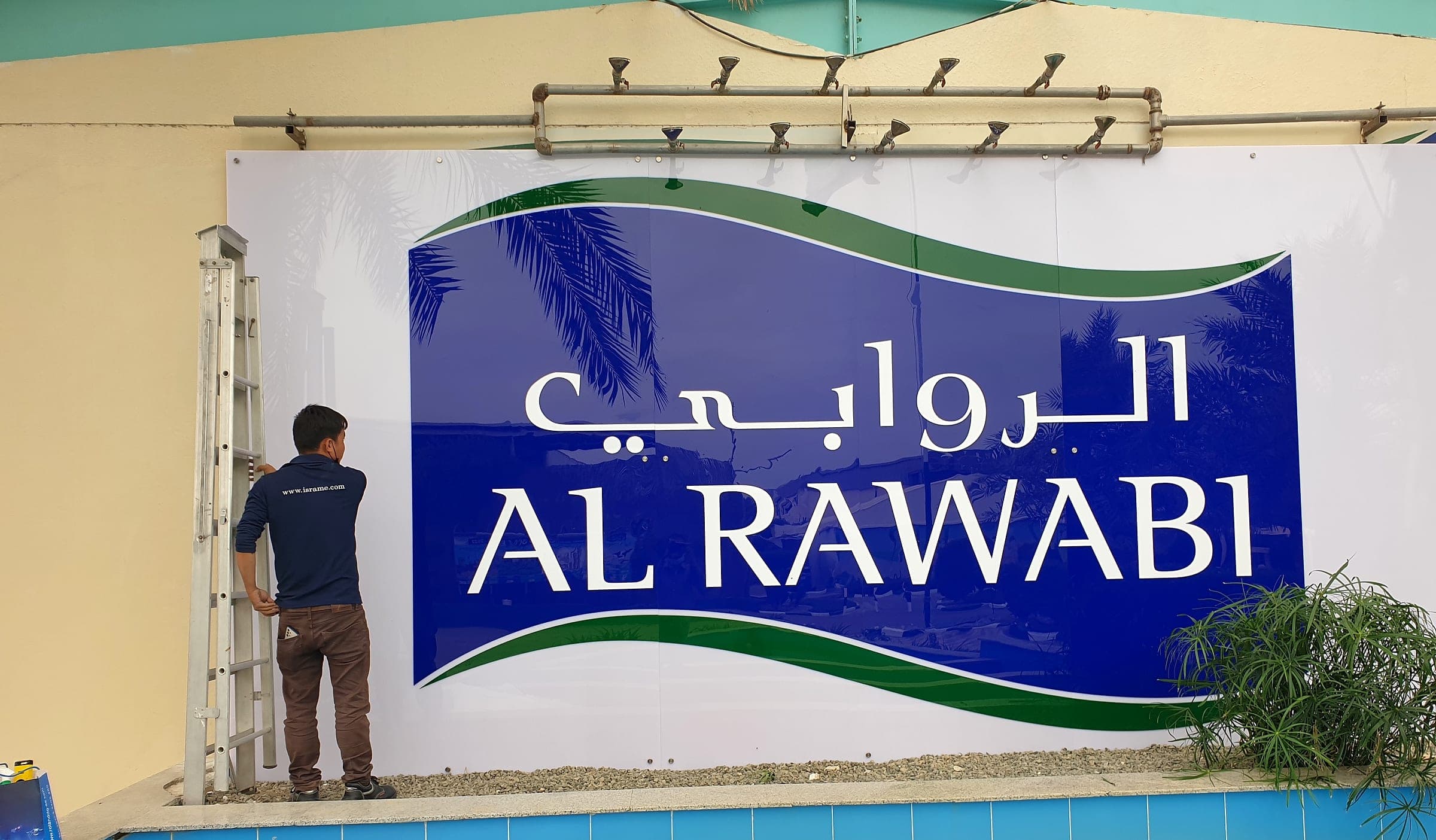 Isra installer fixing a 6 by 3 metre printed Al Rawabi wall sign