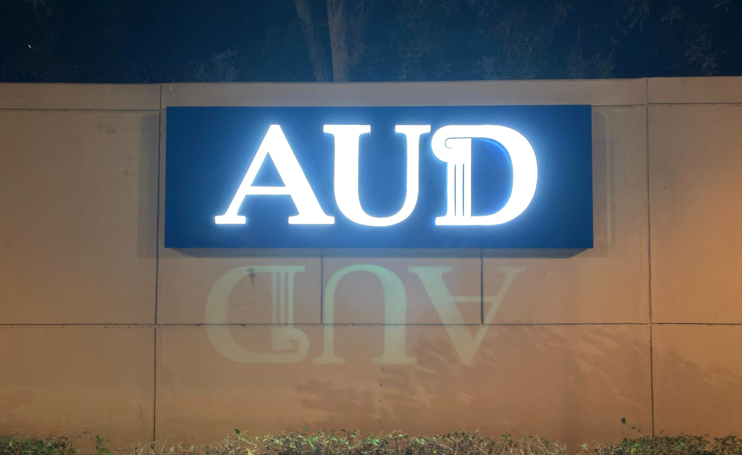 Illuminated AUD monogram letters on a stone boundary wall at night