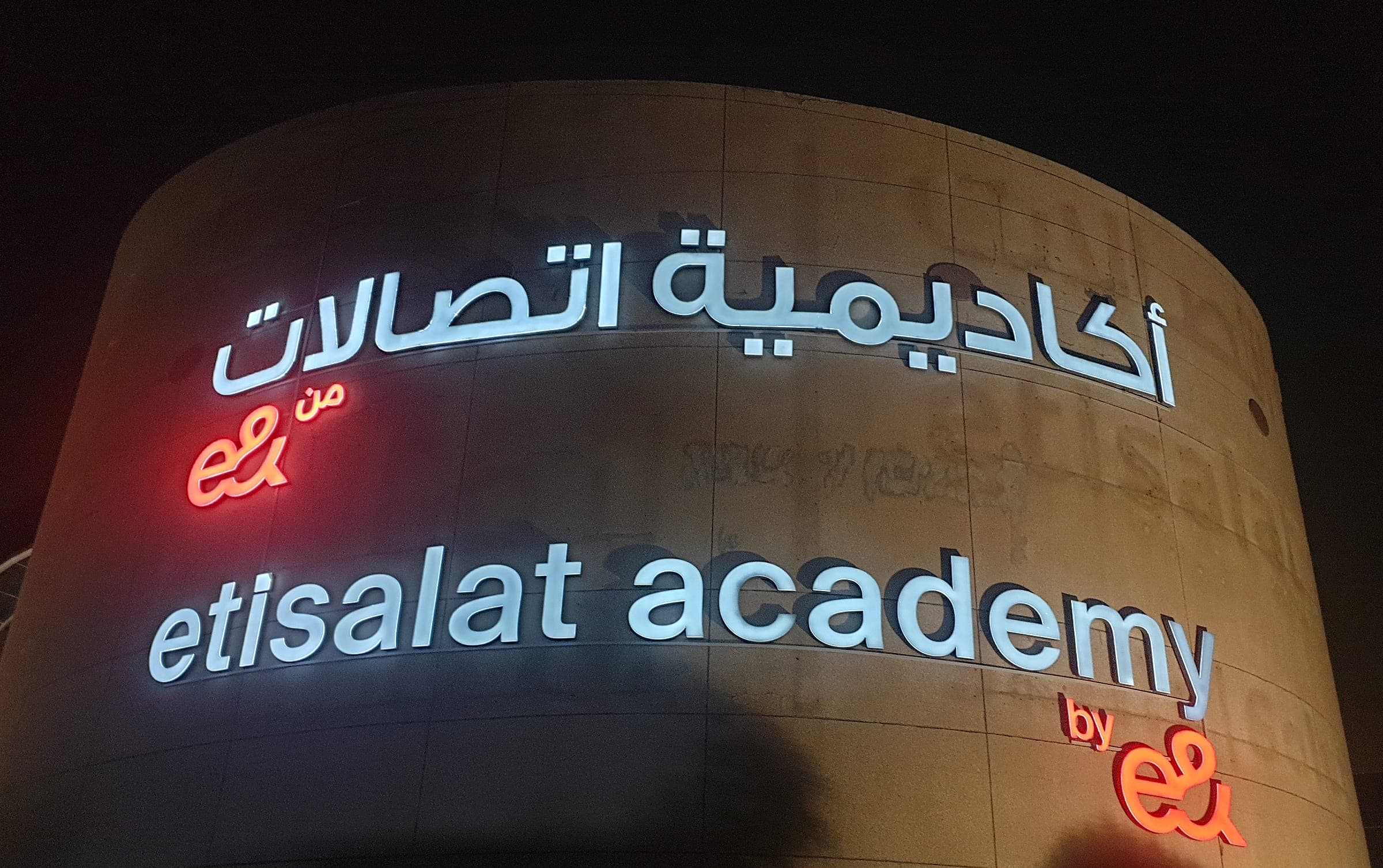 Front-lit channel letters for Etisalat Academy on a curved building at night