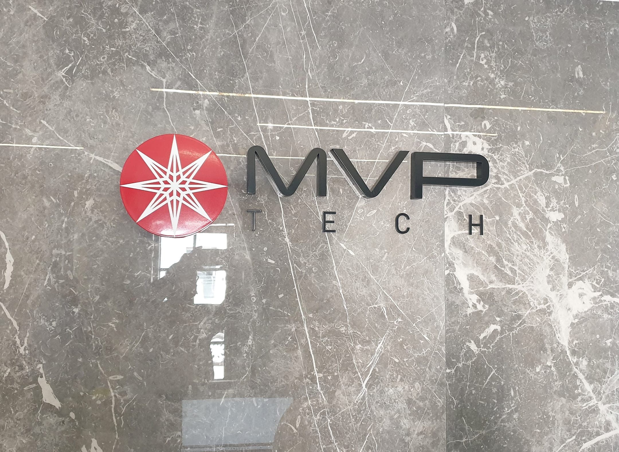 Brushed steel MVP Tech logo and letters on a grey marble reception wall