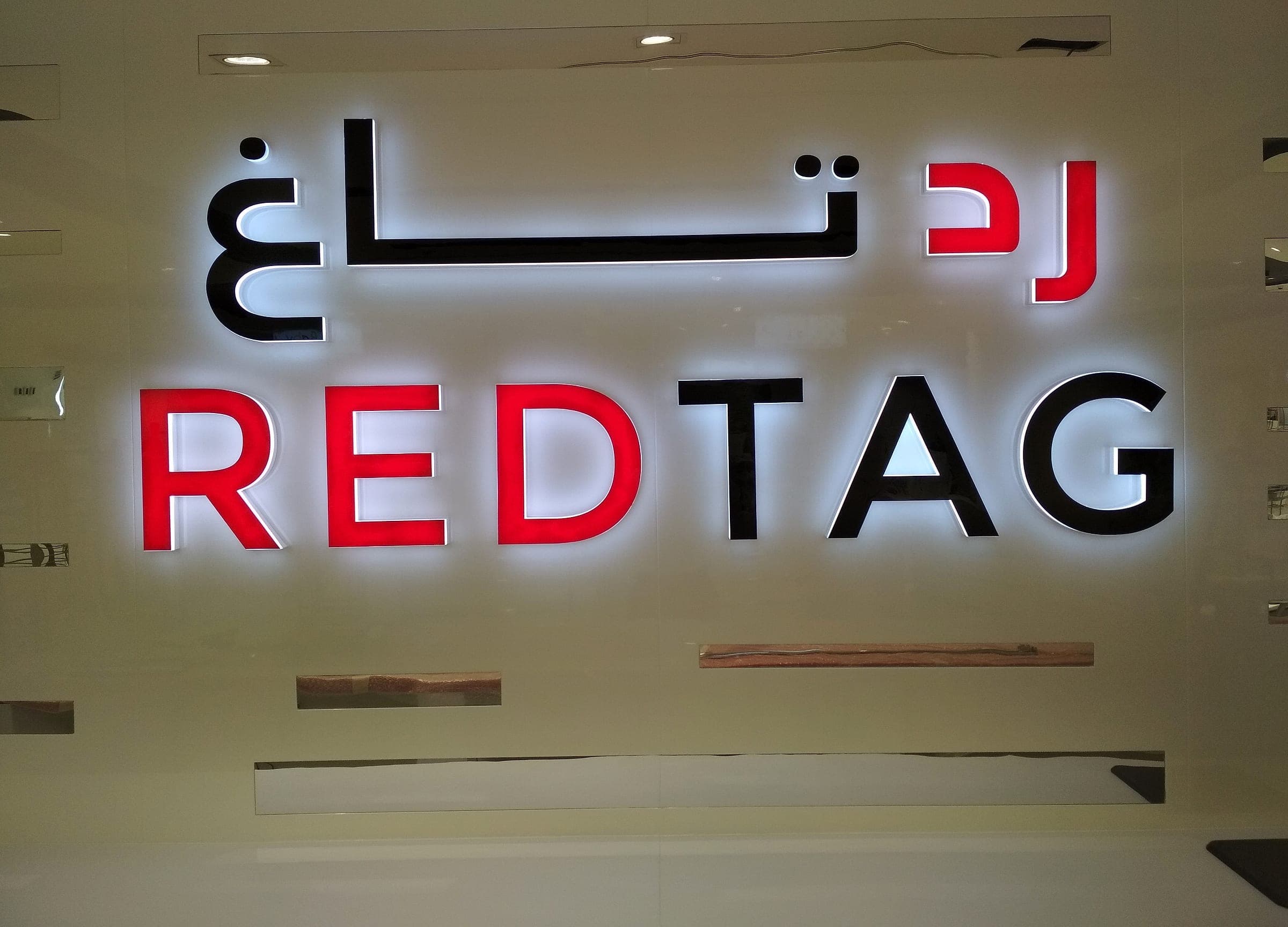 Front-lit and back-lit Redtag letters above a calm feature wall in a Redtag store