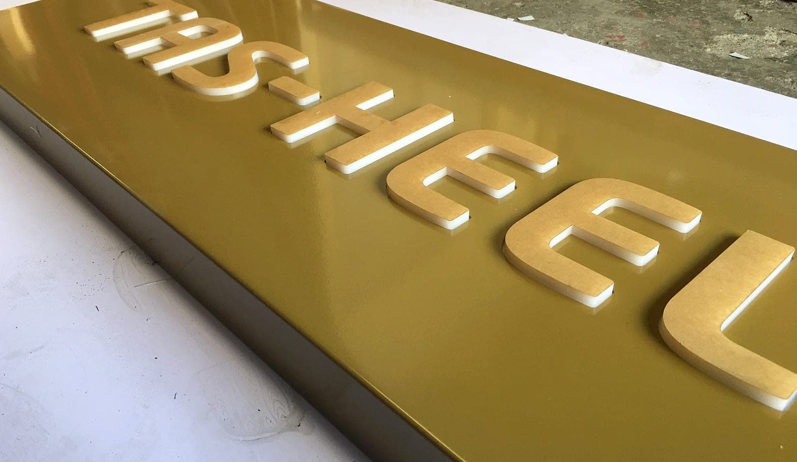 Raised gold acrylic TAS-HEEL letters on a gold panel